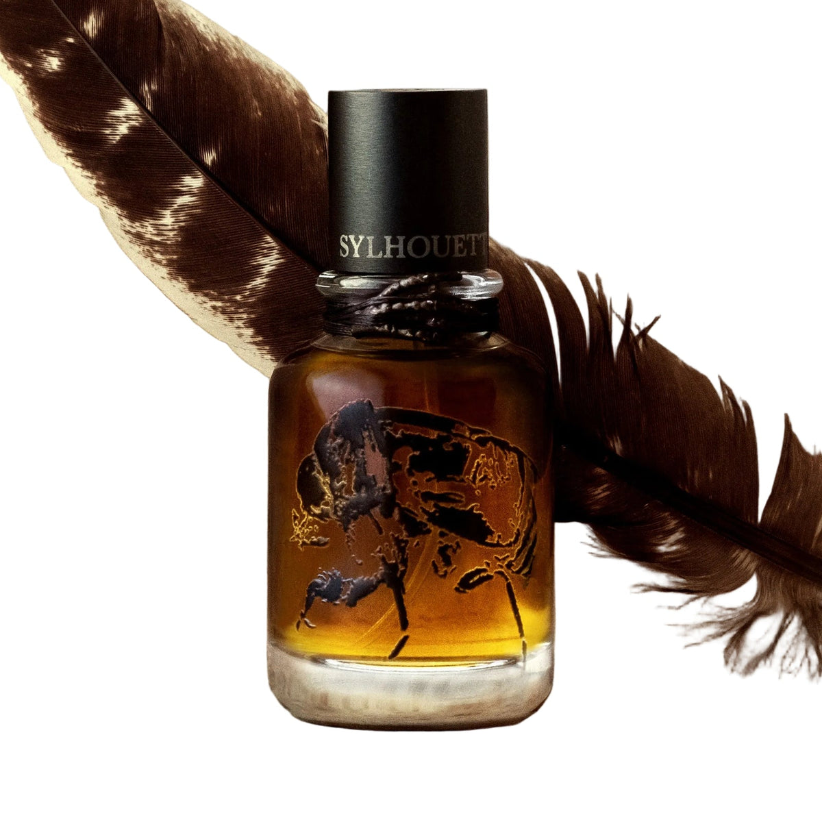 Falj Fel by Sylhouette Parfums, a rounded bottle of dark amber extrait with a black cap and a black etched illustration on the glass, set against a brown and cream feather