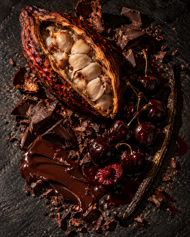 A split cacao pod with dark chocolate, cacao nibs and black cherries on dark stone
