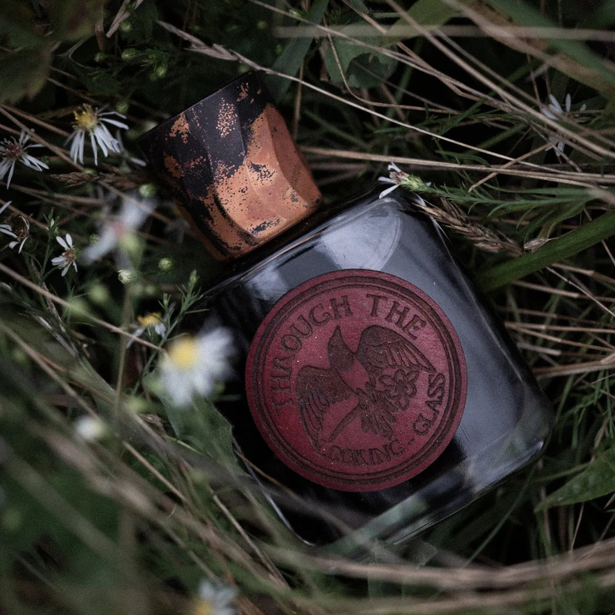 Through the Looking Glass by Folkwinds, the dark glass flask with its copper cap and wax seal, lying in meadow grass